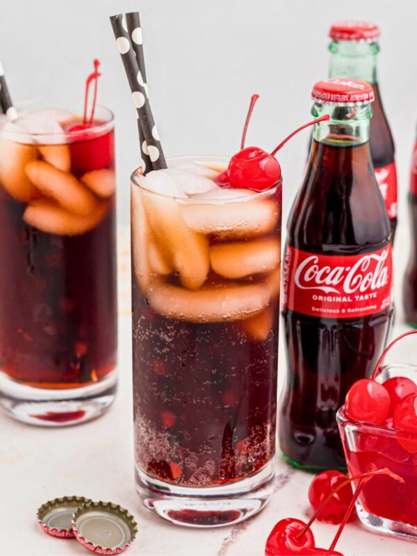 Cola and grenadine mixed in a glass filled with ice, and topped with cherries on a marble table.