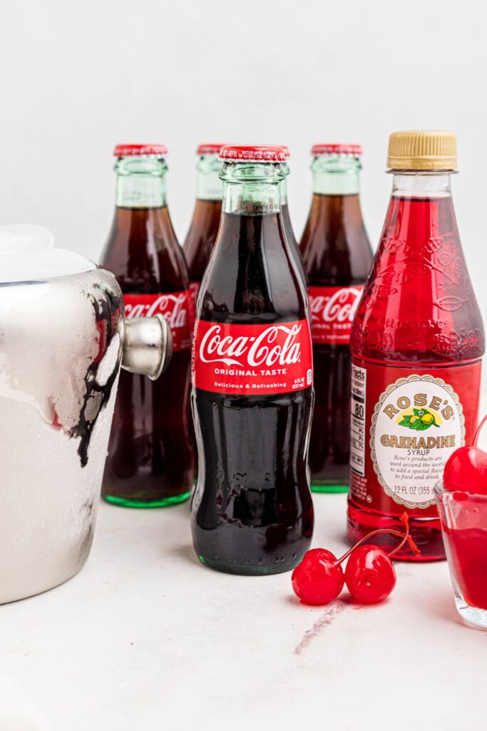 Cola, grenadine syrup, cherries, and ice on a marble table. 