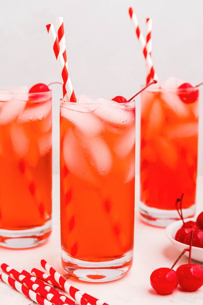 Bright red Shirley Temple drinks in tall glasses with straws and cherries. 