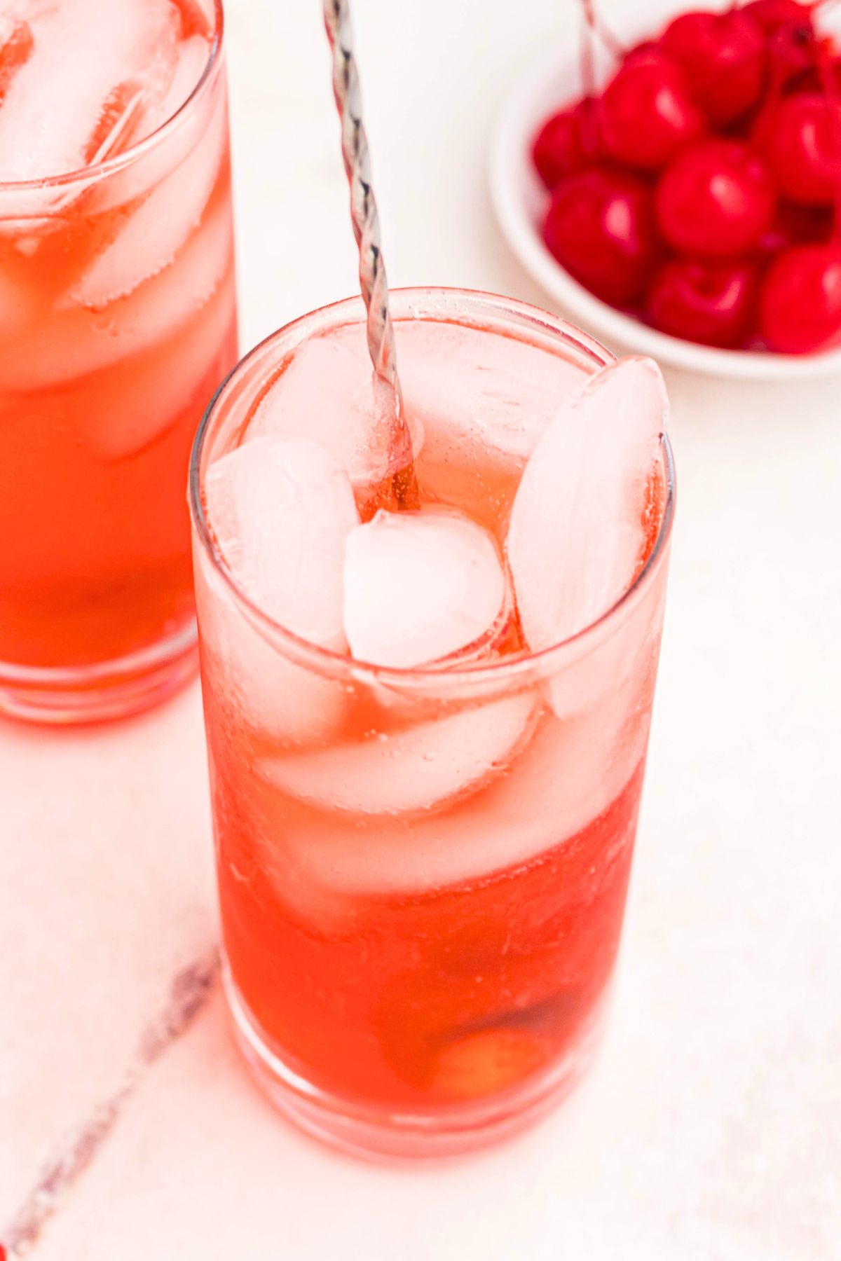 Bright red drink in a tall glass with ice and cherries on the table.