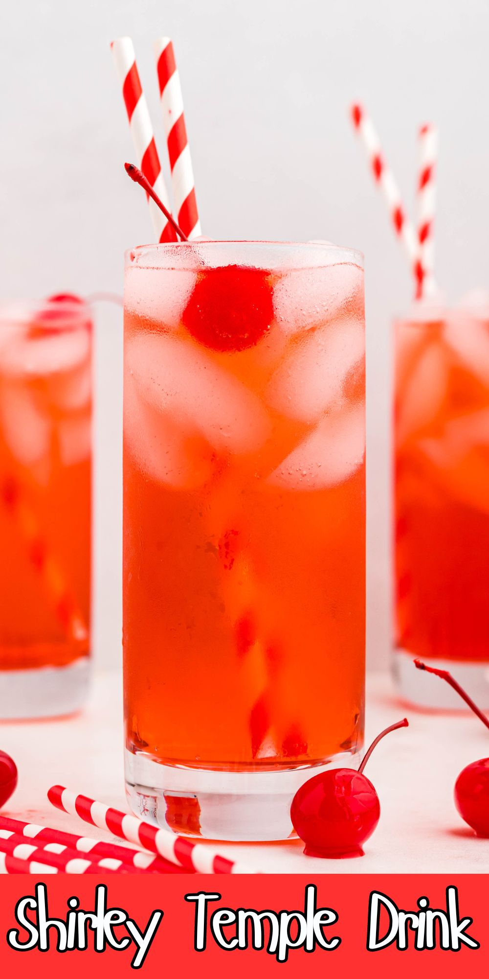 Bright red drink in a tall glass with ice and cherries on the table.