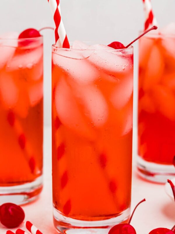 Bright red drink in a tall glass with ice and cherries on the table.