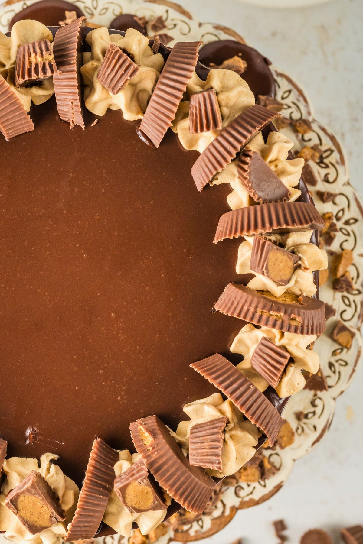 Top view of a frosted cake with chocolate ganache on top with peanut butter cups for decoration. 