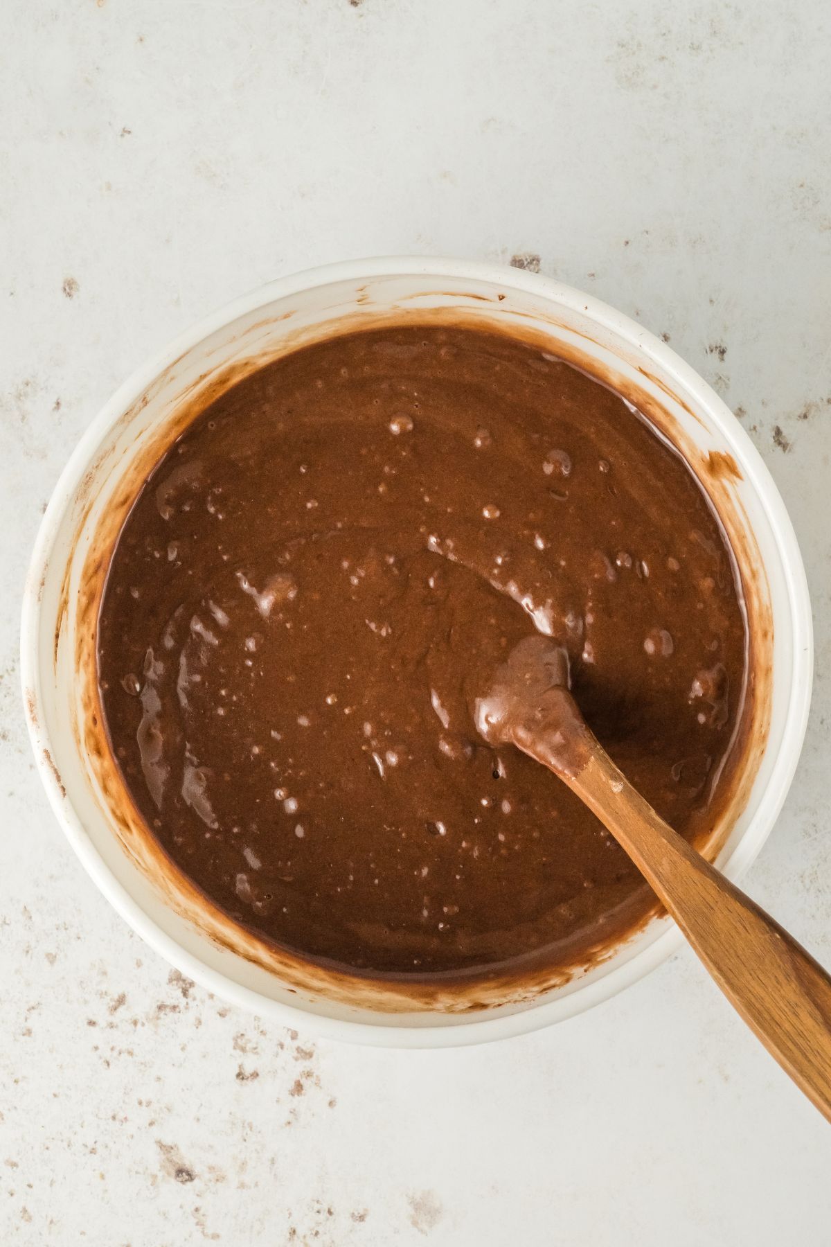 Chocolate cake batter in a large bowl being mixed with a spoon. 