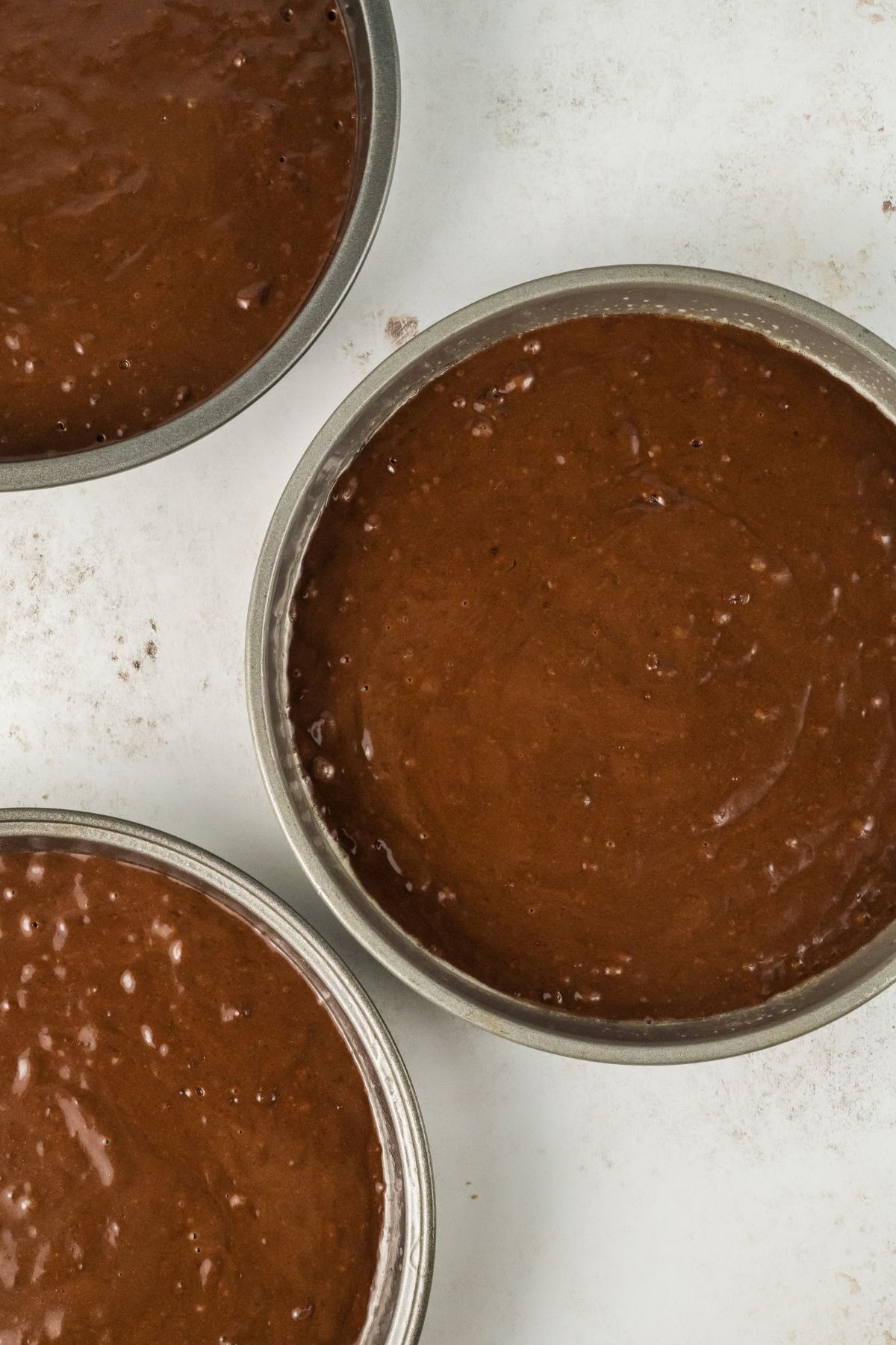 Three cake pans filled with chocolate cake batter before being baked. 