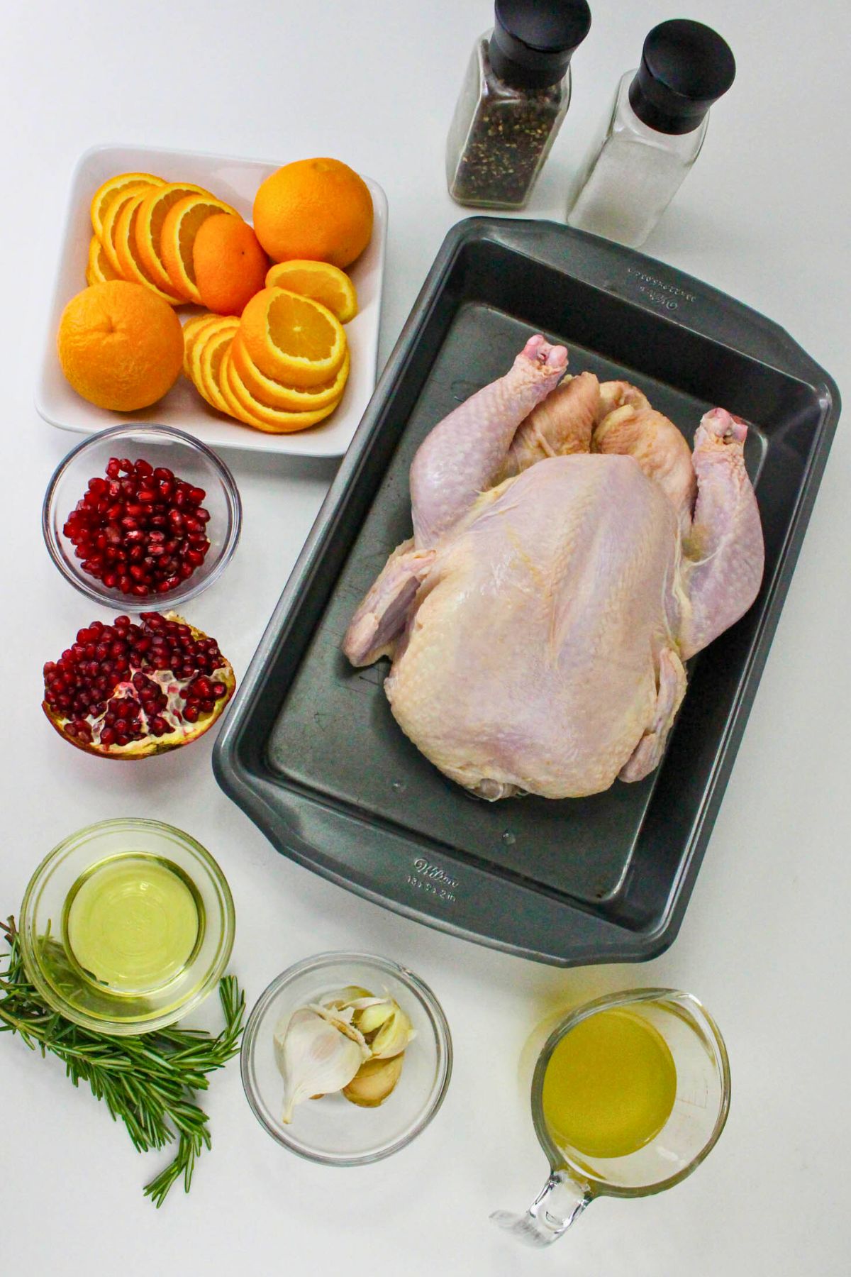 An uncooked whole chicken with other ingredients measured out on a marble table. 