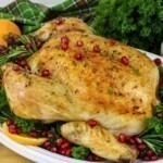 Golden roasted chicken on a white platter with parsley and pomegranate seeds as garnish.