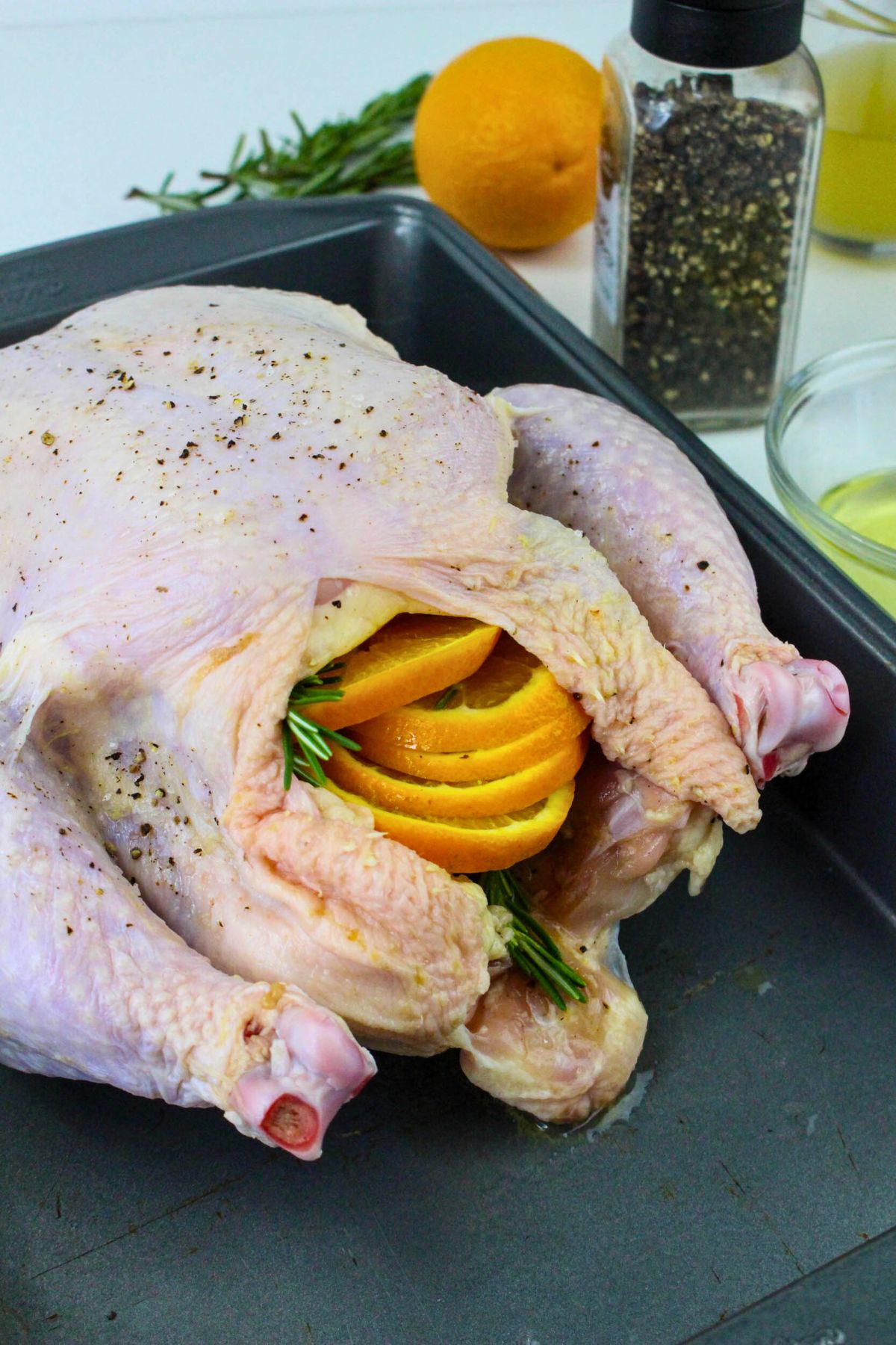 Uncooked chicken stuffed with orange slices and seasonings in a roasting pan. 