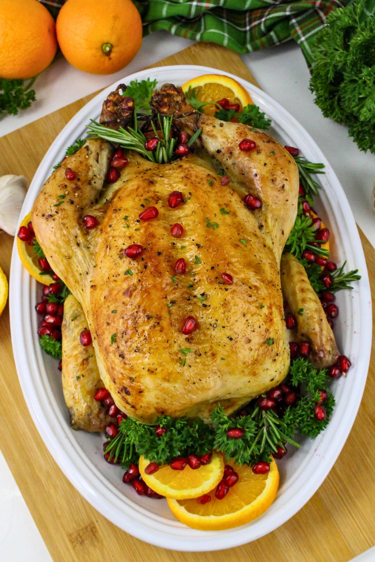 Golden roasted chicken on a white platter with parsley and pomegranate seeds as garnish. 