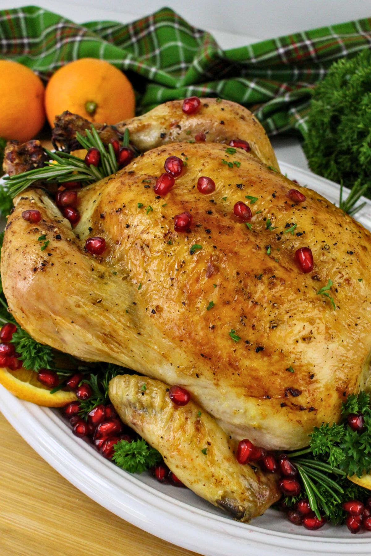 Golden brown roasted chicken on a platter with pomegranate seeds and oranges as garnish. 