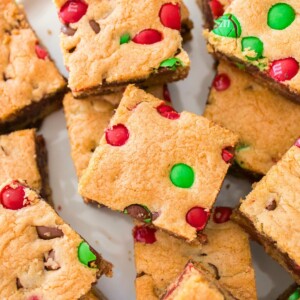 Golden square Christmas cookie bars with red and green candies baked in, stacked on a table.