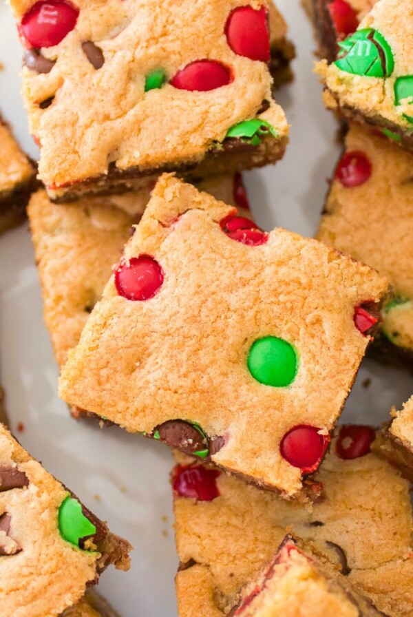 Golden square Christmas cookie bars with red and green candies baked in, stacked on a table.