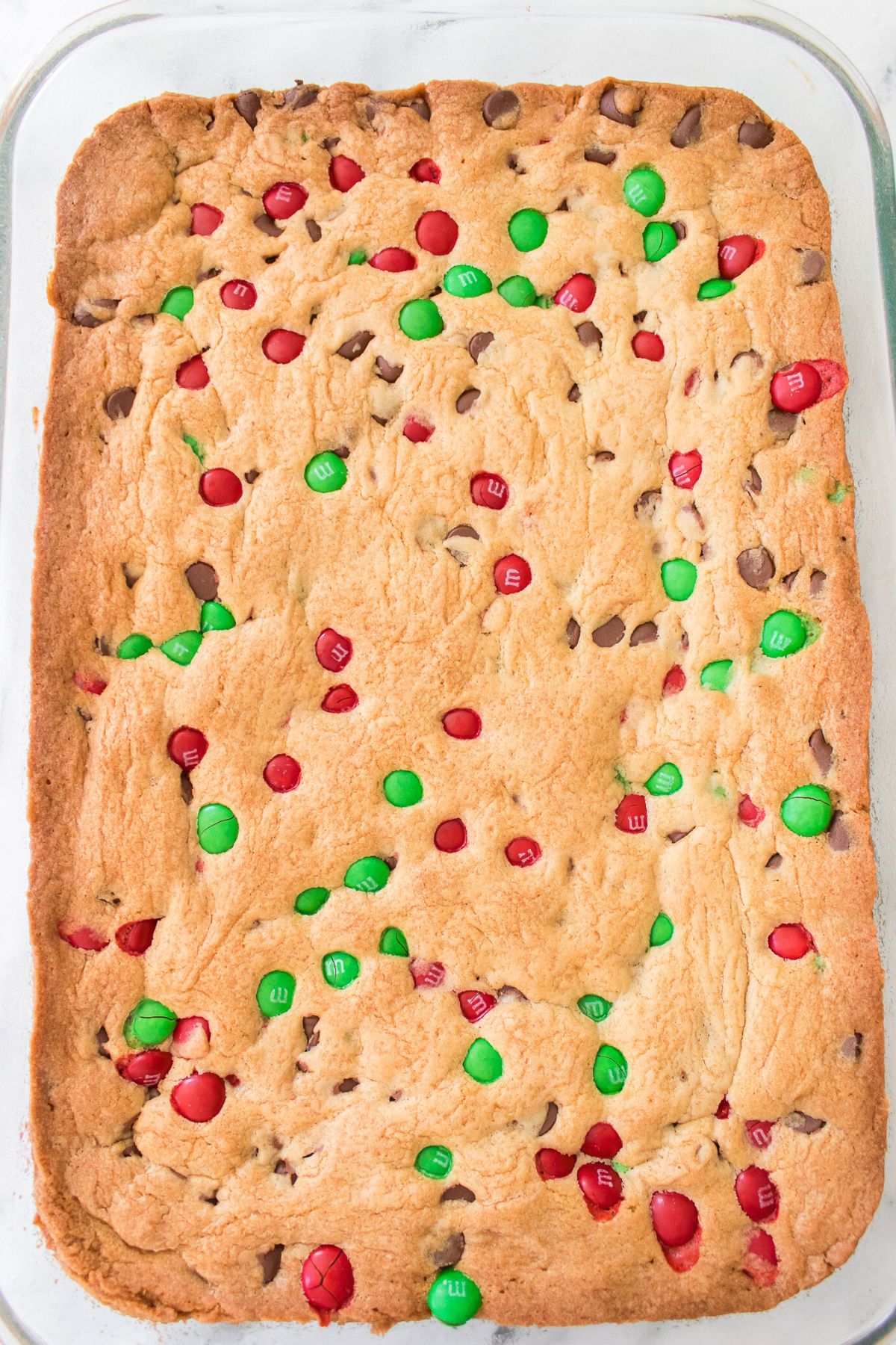 Golden brown baked m and m cookie dough in a clear glass baking dish. 