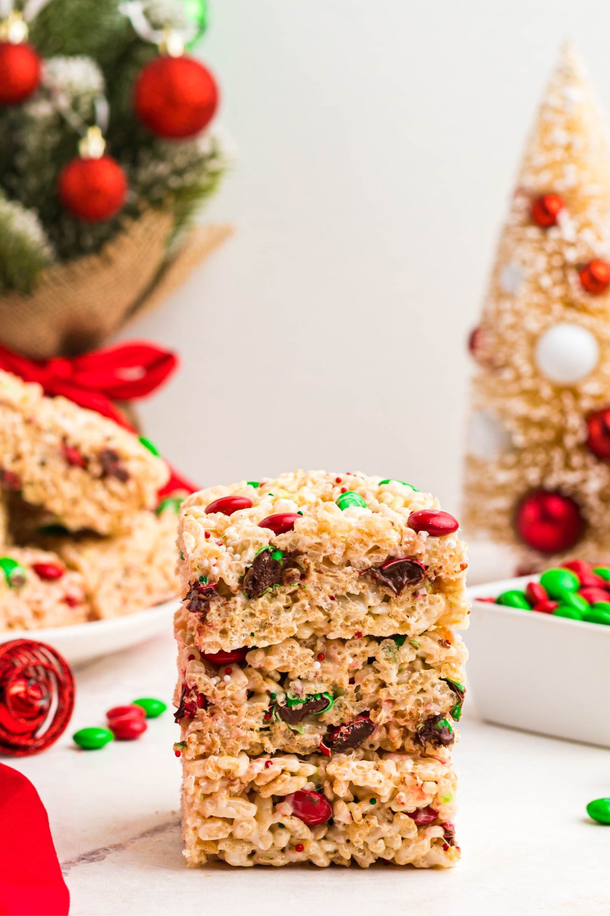 Christmas rice krispie treats stacked on a marble table with a Christmas tree behind them. 