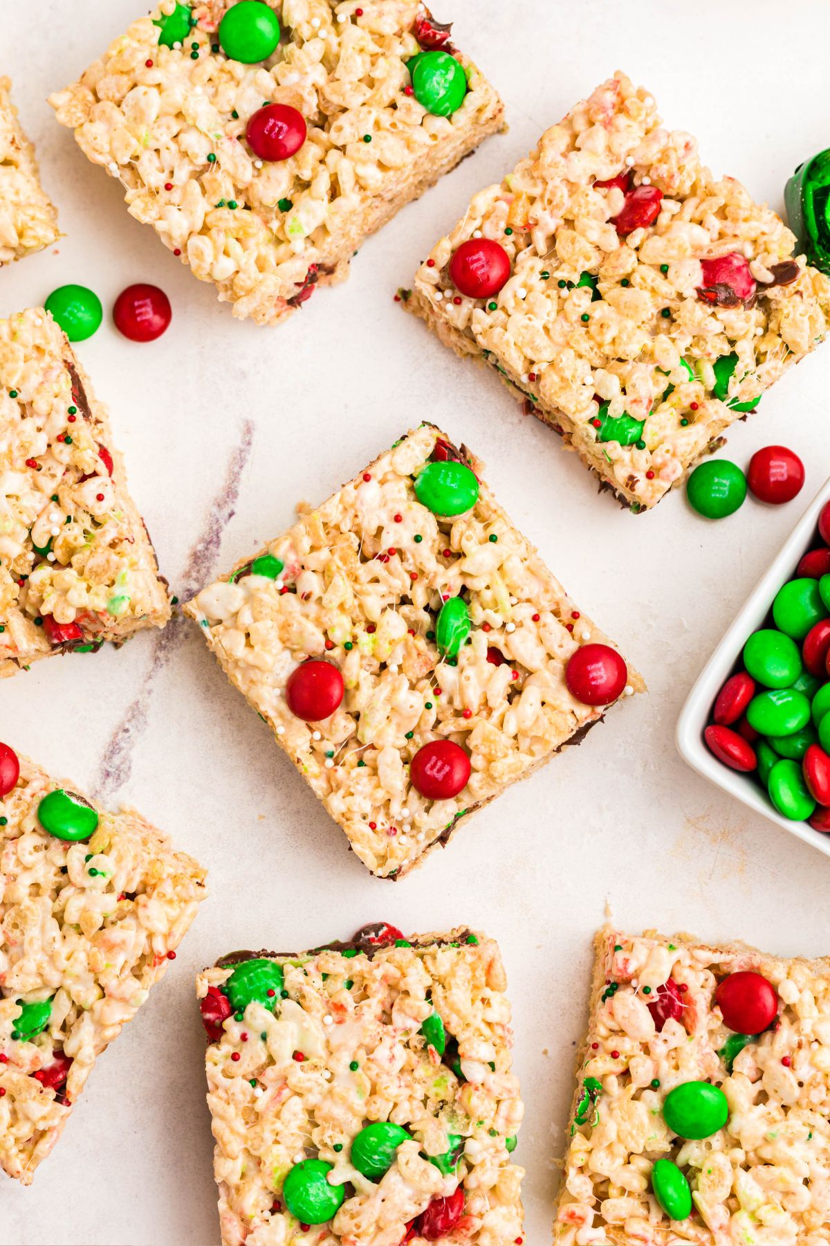 Rice krispie treats with red and green m and m's mixed in, cut into squares, laid out on a marble table. 