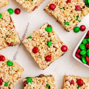 Rice krispie treats with red and green m and m's mixed in, cut into squares, laid out on a marble table.