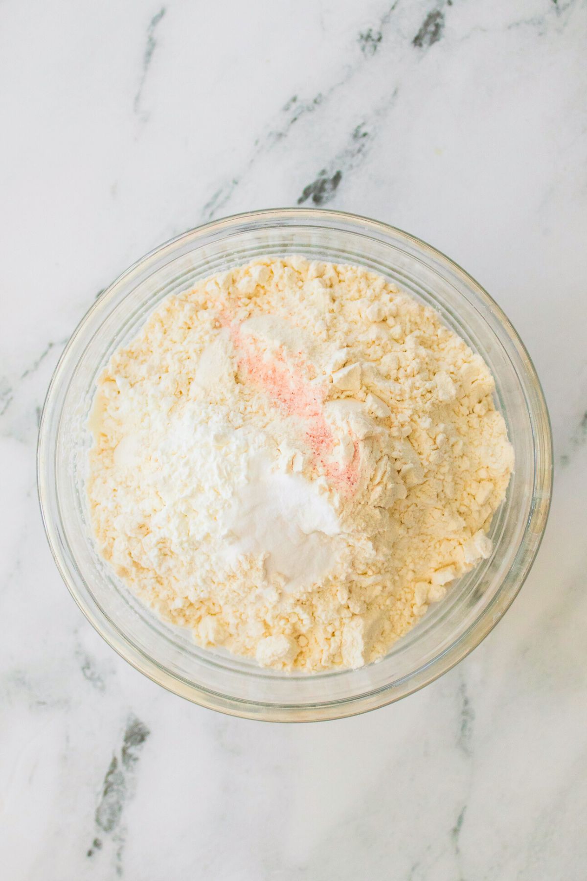 Dry ingredients being mixed together in a large clear glass bowl. 