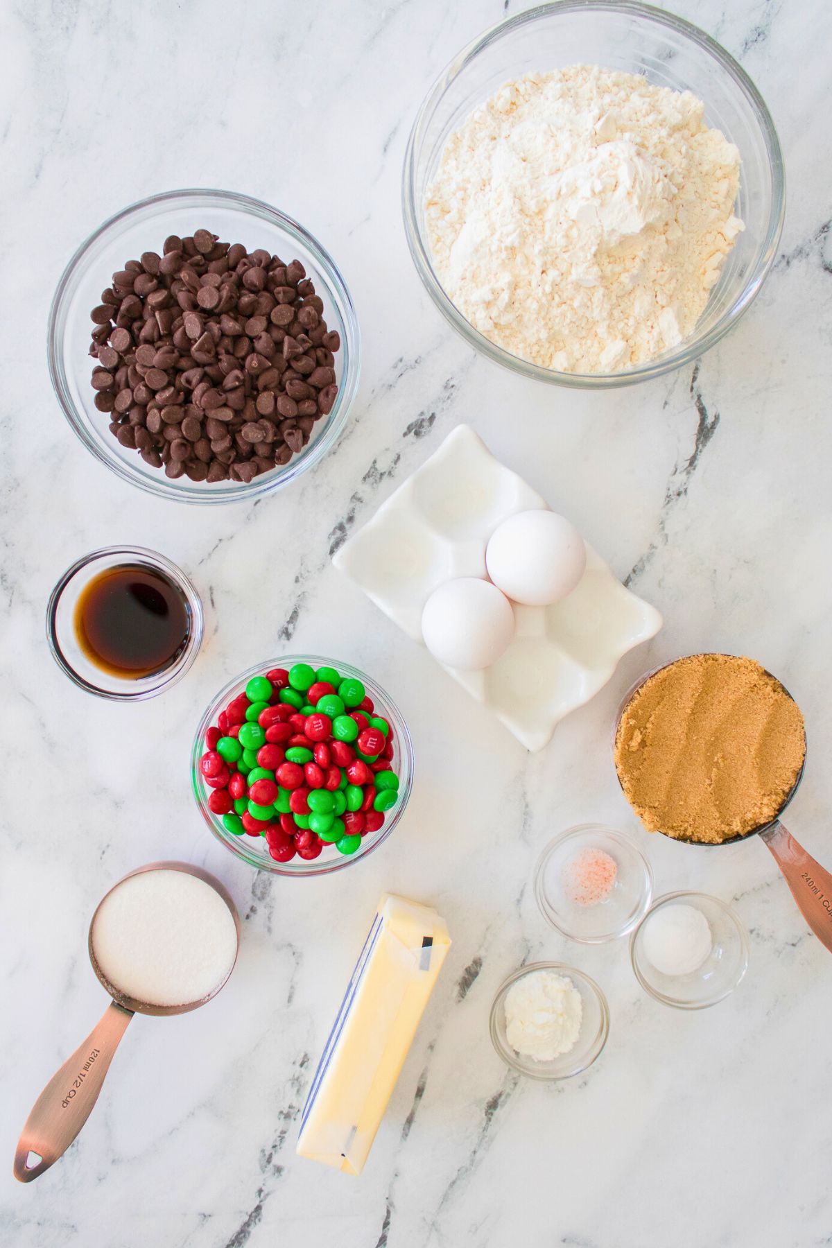 Ingredients needed to make cookie bars, measured in containers on a white marble board. 