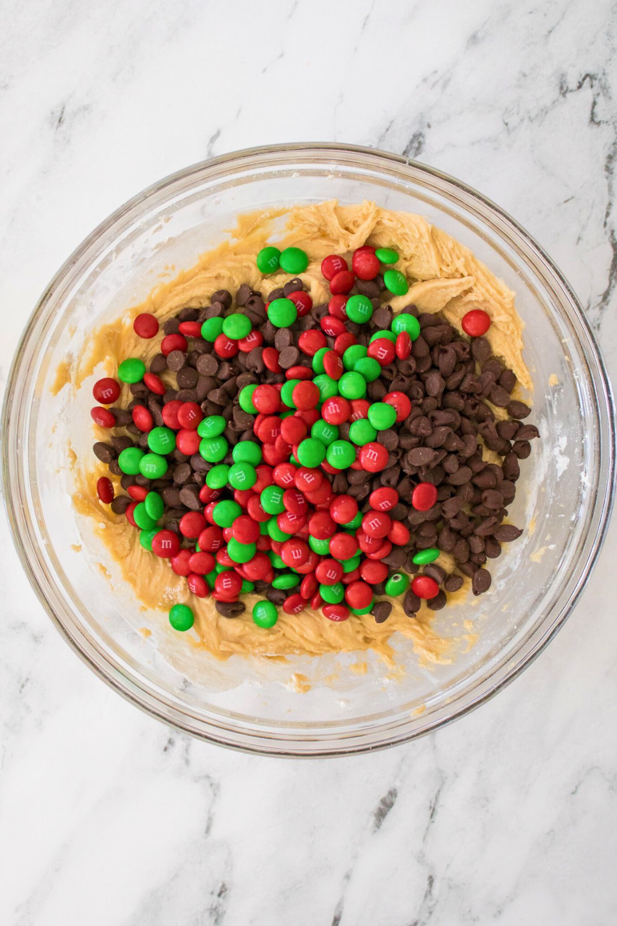 Chocolate chips and m and m's being folded into sugar cookie dough. 