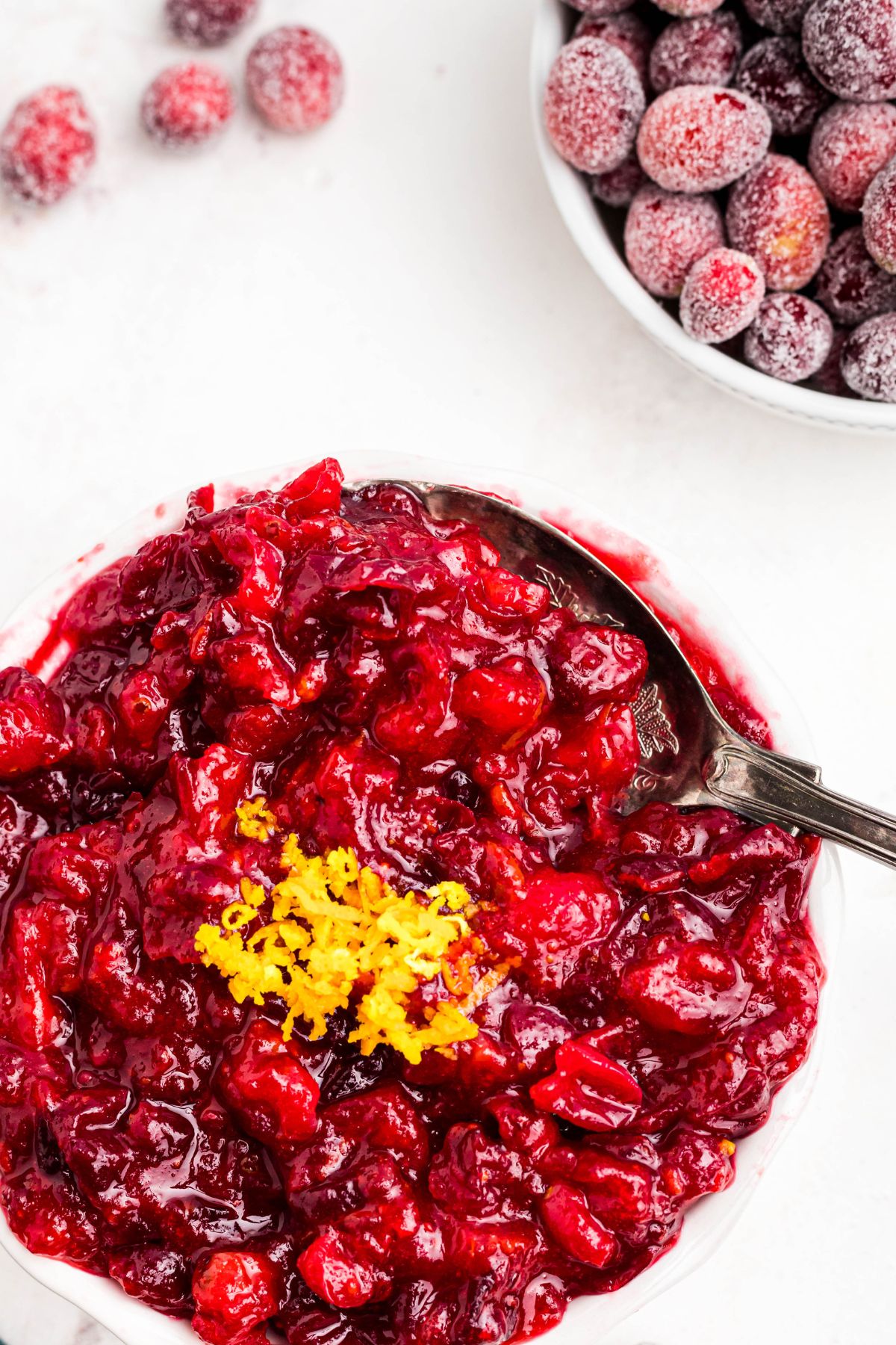 A large silver spoon scooping out cranberry sauce in a white bowl. 