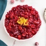 Bright red cranberry sauce in a white bowl, topped with orange zest as a garnish.