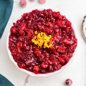 Bright red cranberry sauce in a white bowl, topped with orange zest as a garnish.