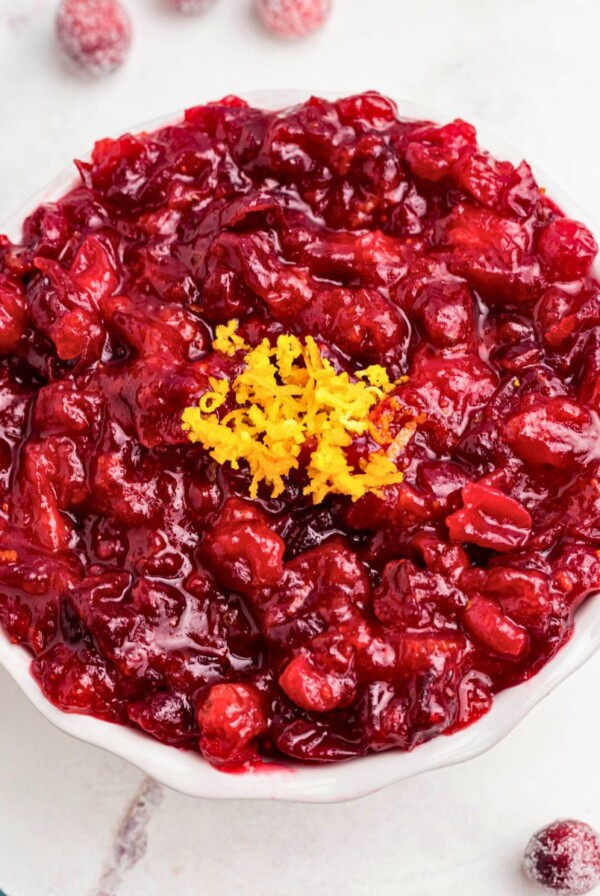 Bright red cranberry sauce in a white bowl, topped with orange zest as a garnish.