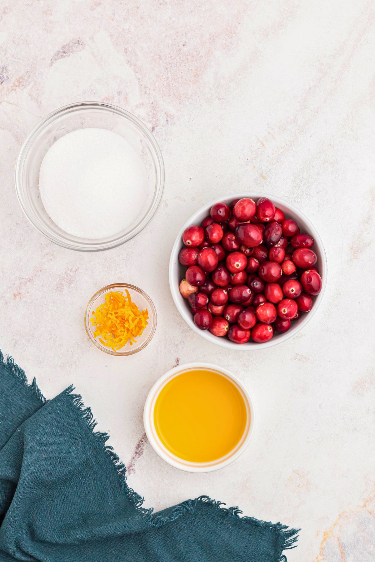 Cranberries, orange juice, orange zest, and sugar, on a marble table. 