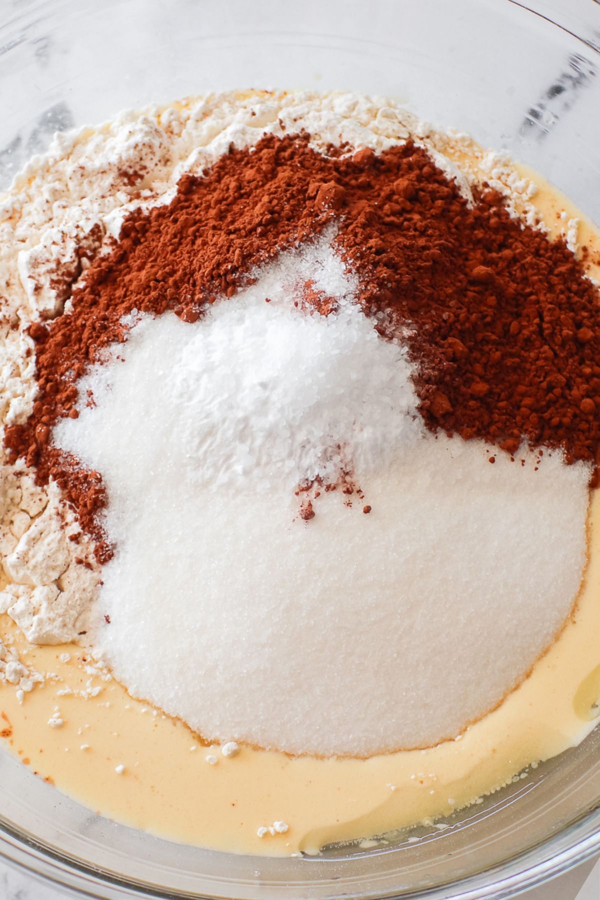 Sugar, cocoa powder, and other ingredients in a large clear glass bowl. 