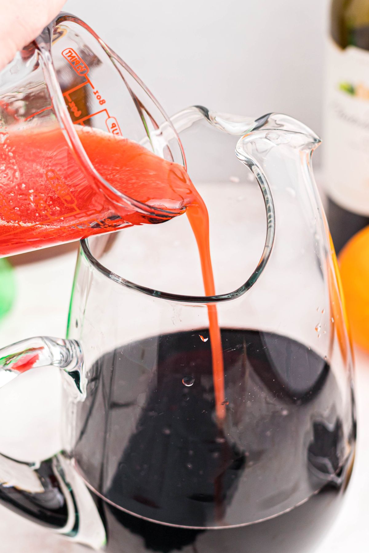 Cranberry and sugar juices being added to merlot in a clear pitcher.