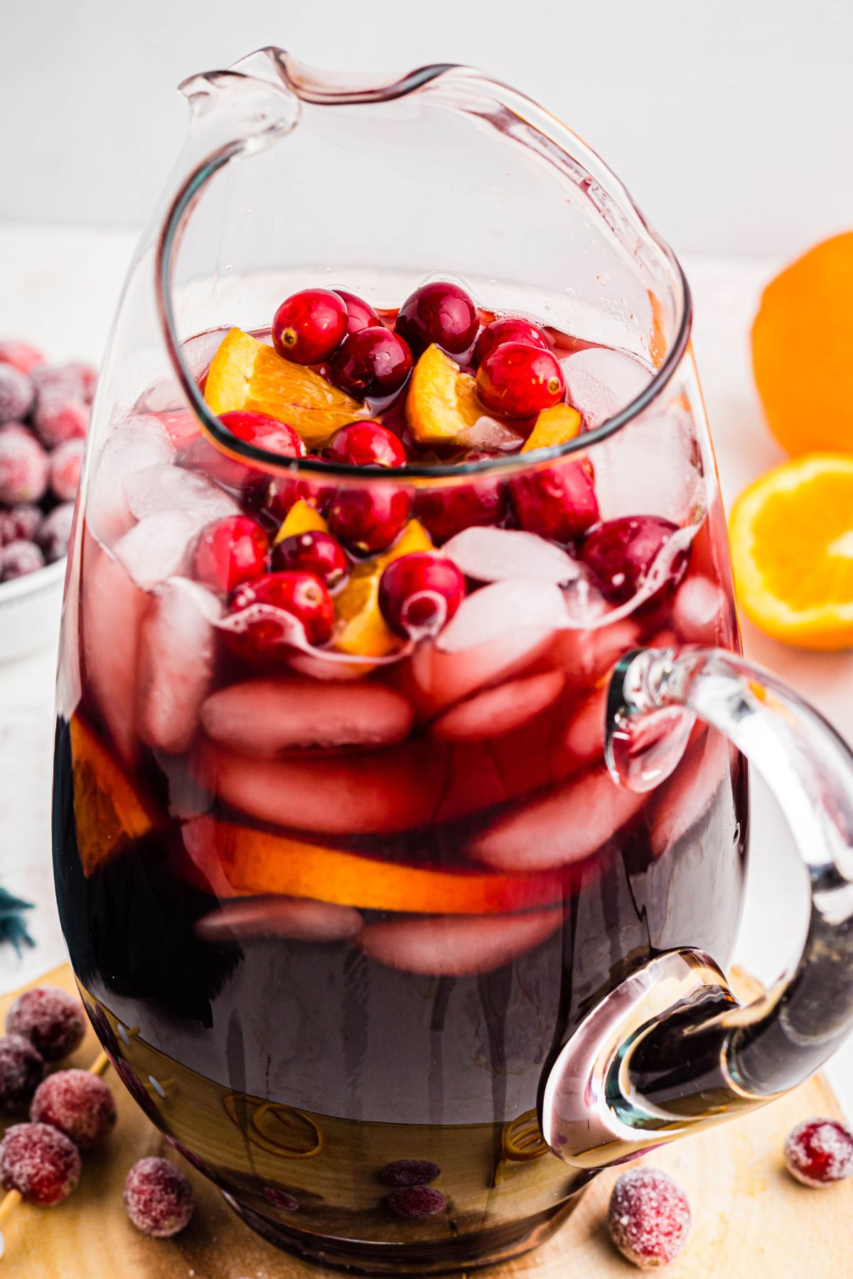 Sangria in a clear pitcher with cranberries and orange pieces mixed into the wine. 