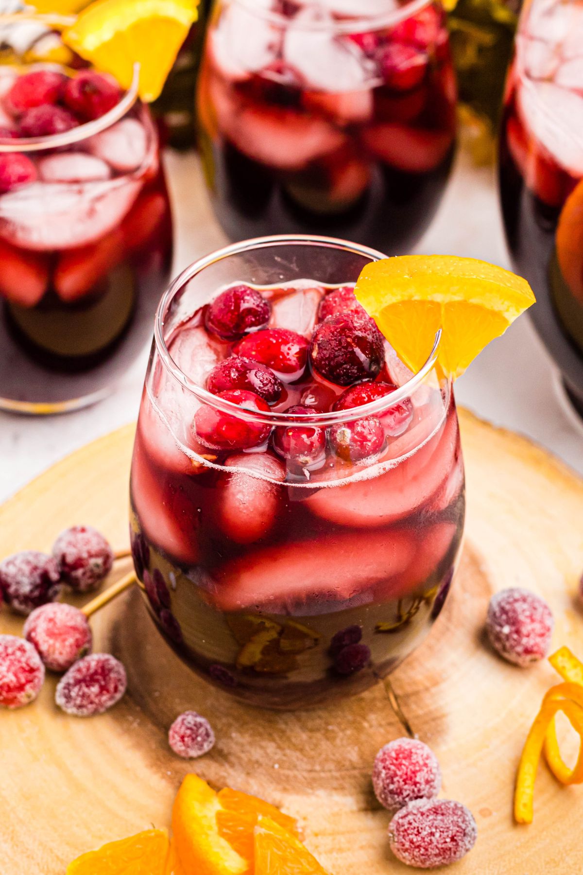 Stemless wine glass filled with homemade sangria, ice, cranberries, and orange slices.