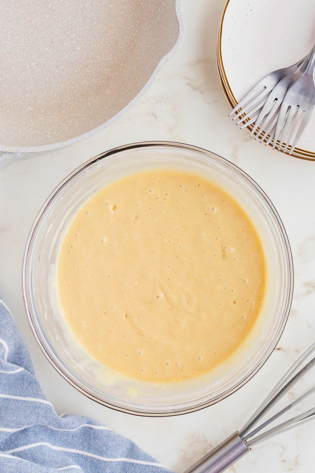 Gluten free pancake batter in a large clear glass bowl in front of the skillet. 