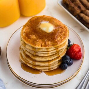 Golden gluten free pancakes stacked on a white plate.