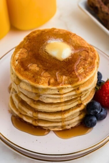 Golden gluten free pancakes stacked on a white plate.