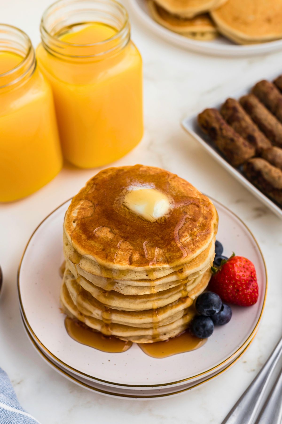 Light and fluffy golden pancakes stacked on a white plate with berries and syrup. 