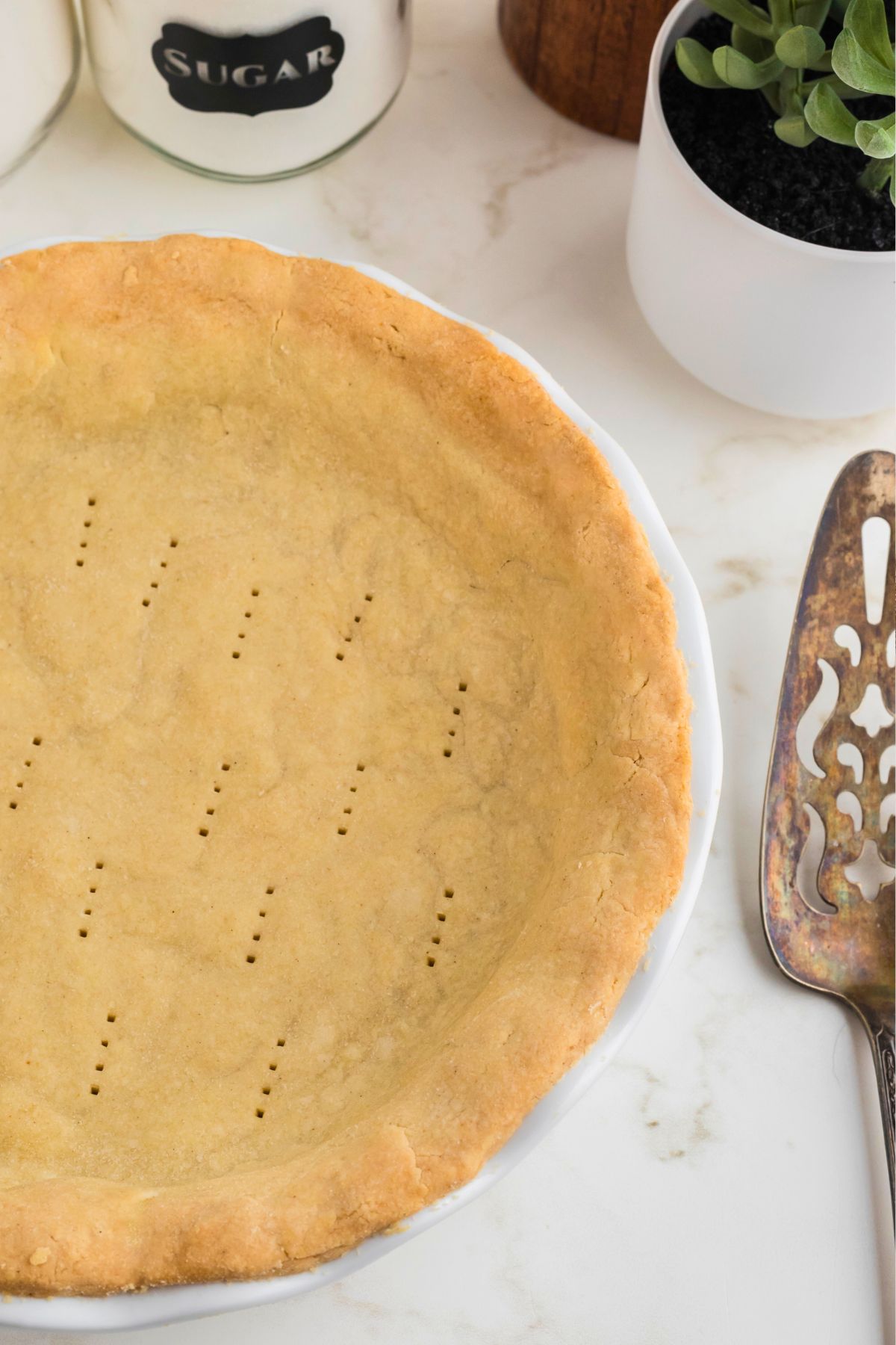 Golden brown baked pie crust in a white pie plate on a marble table.