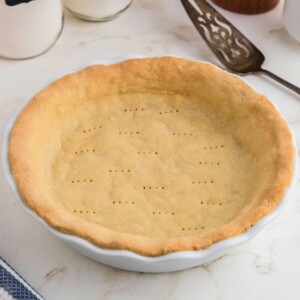 Golden brown baked pie crust in a white pie plate on a marble table.