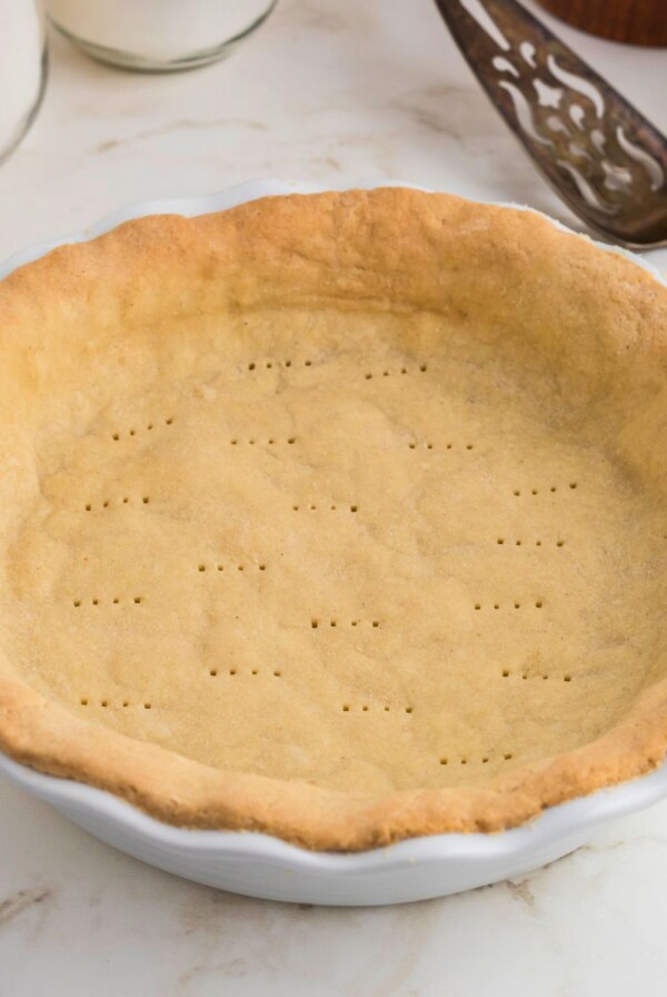 Golden brown baked pie crust in a white pie plate on a marble table.