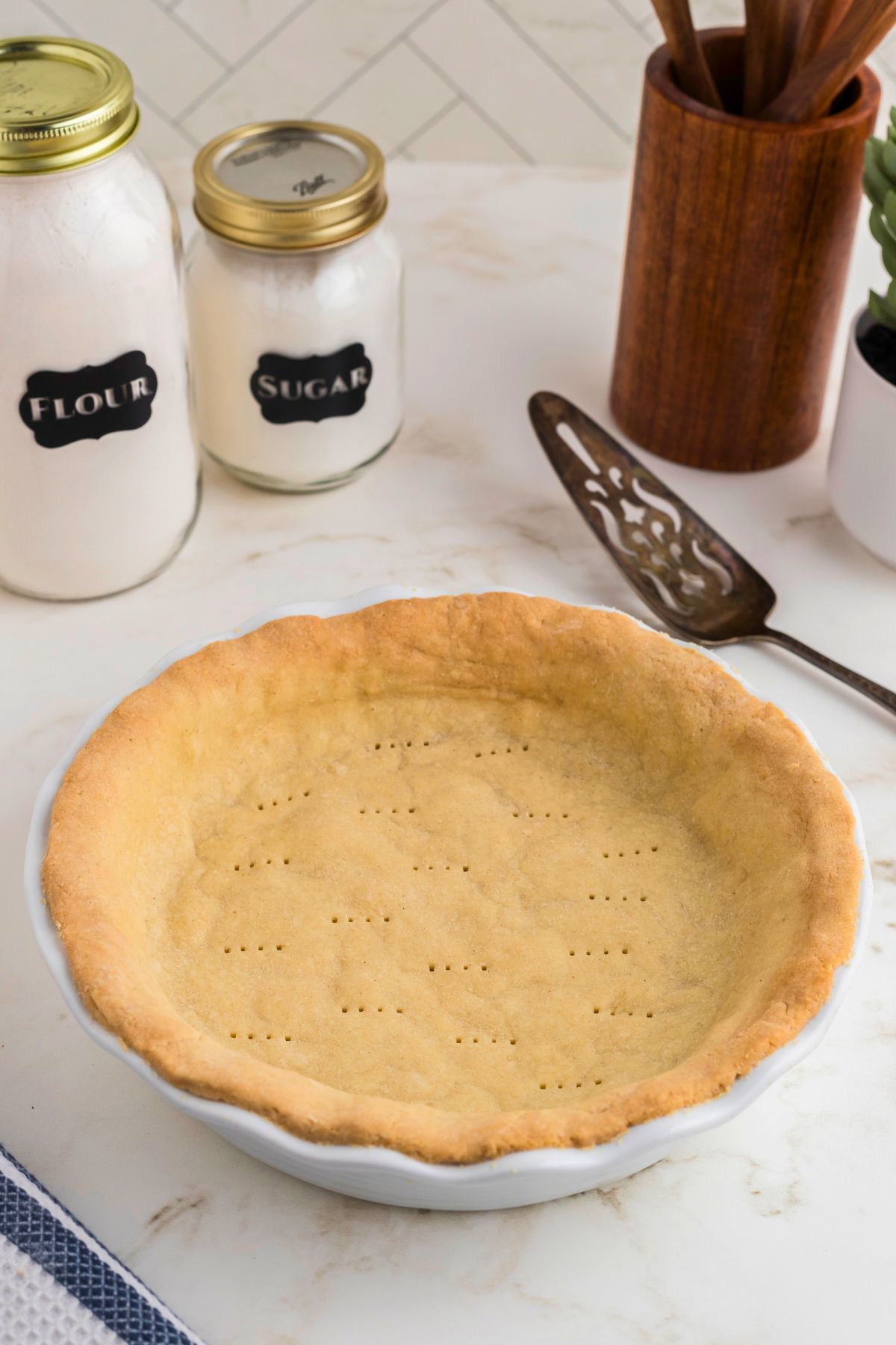 Golden brown baked pie crust in a white pie plate on a marble table. 