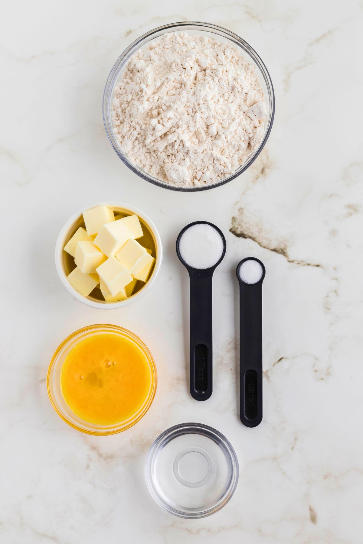 Ingredients needed to make pie crust measured out onto marble table. 