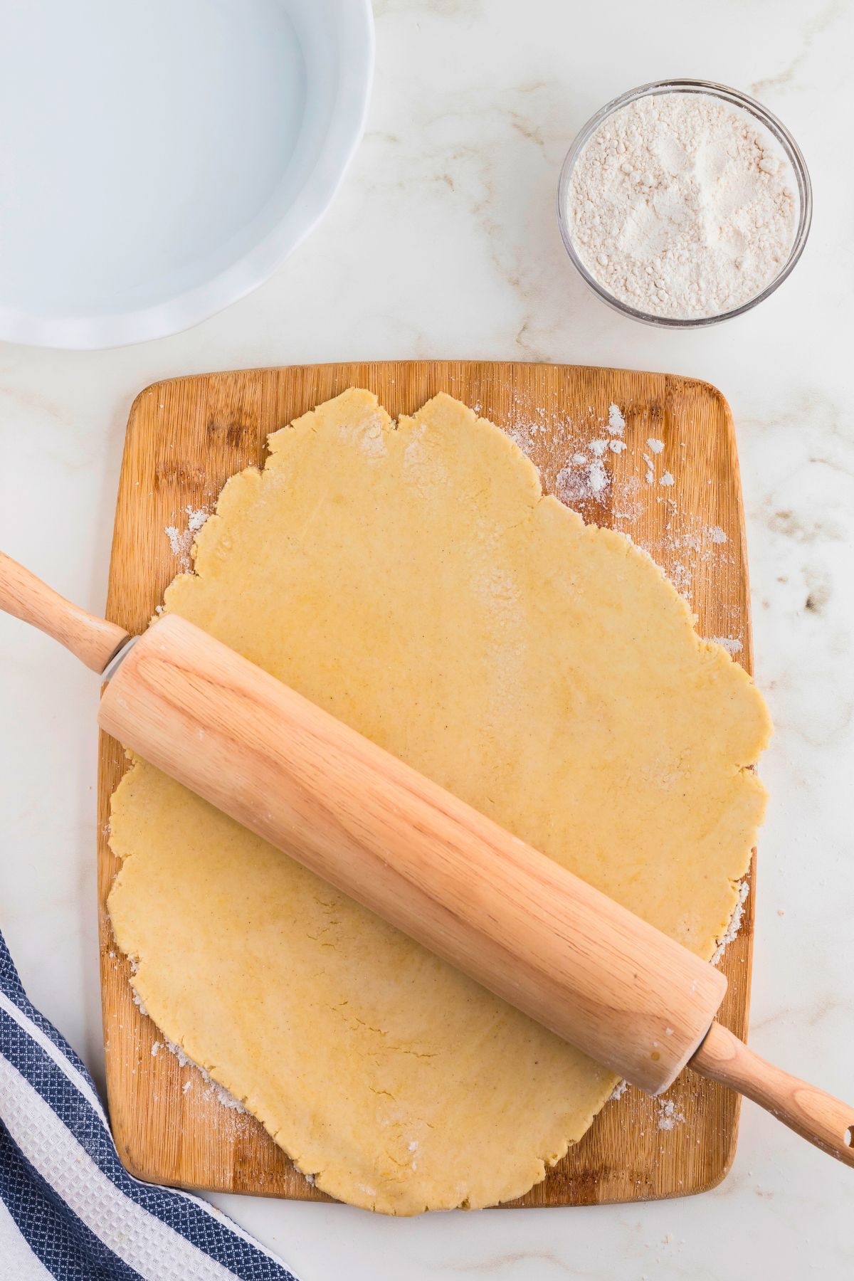 Light golden raw pie crust dough rolled out with a wooden rolling pin. 