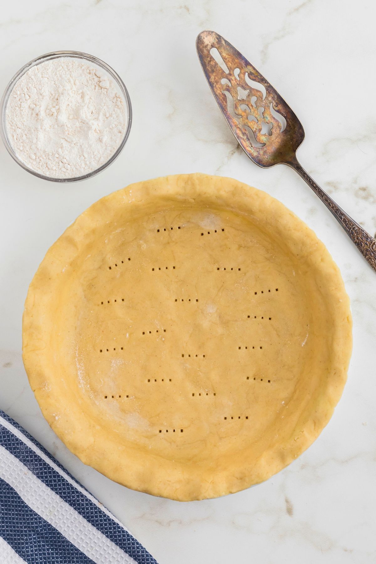 Uncooked pie dough rolled out in a pie dish with fork holes poked in the bottom. 