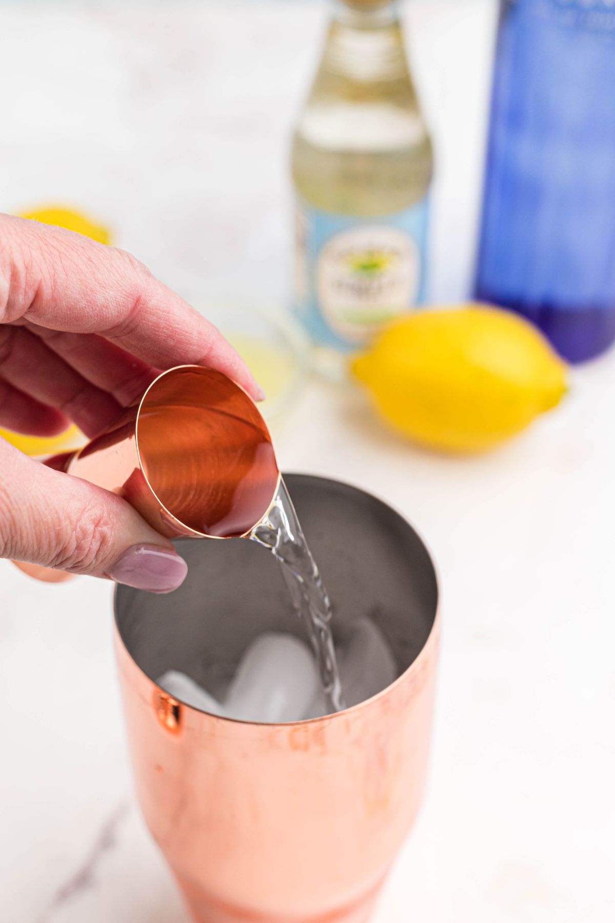 Vodka being poured into cocktail shaker filled with ice. 