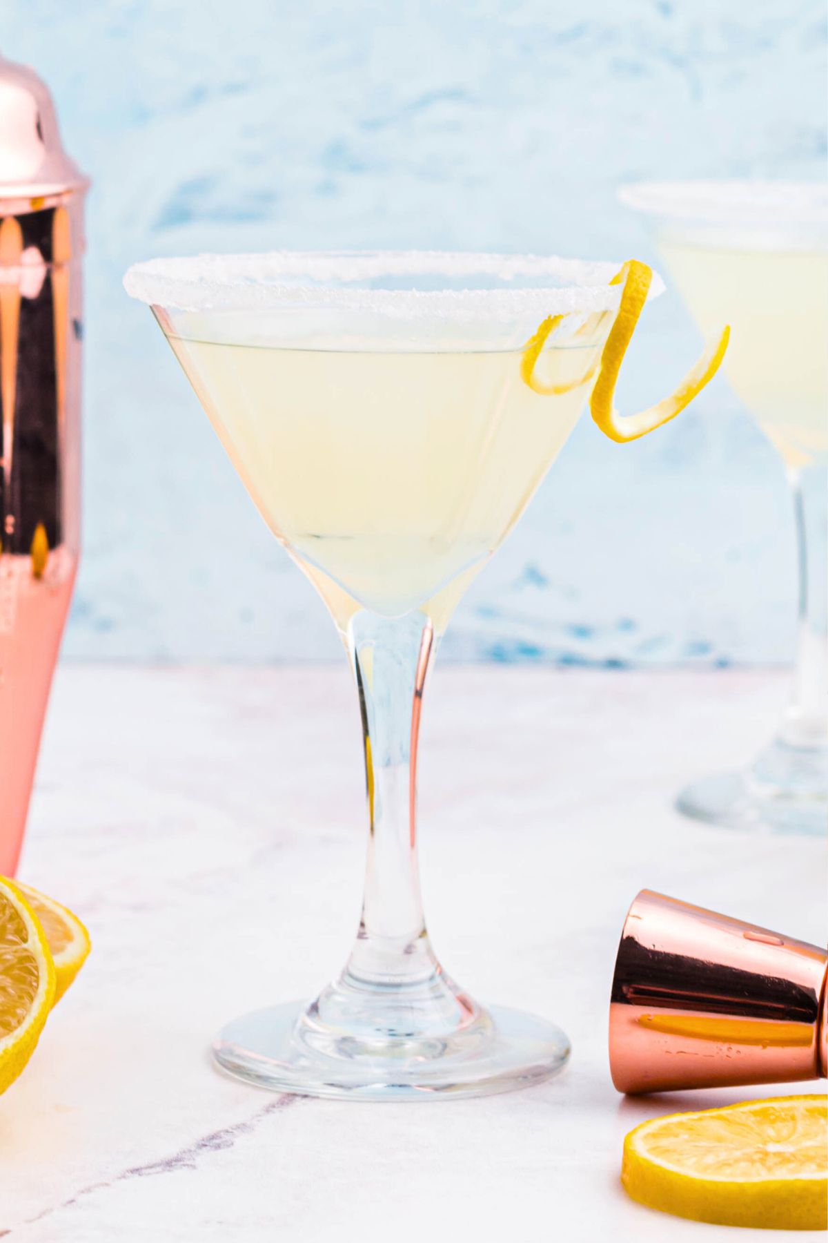 Light yellow lemon drop martini in a glass with a lemon curl garnish. 