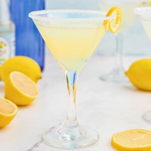 Lemon drop martini in a martini glass on a marble table with lemon slices on the table.