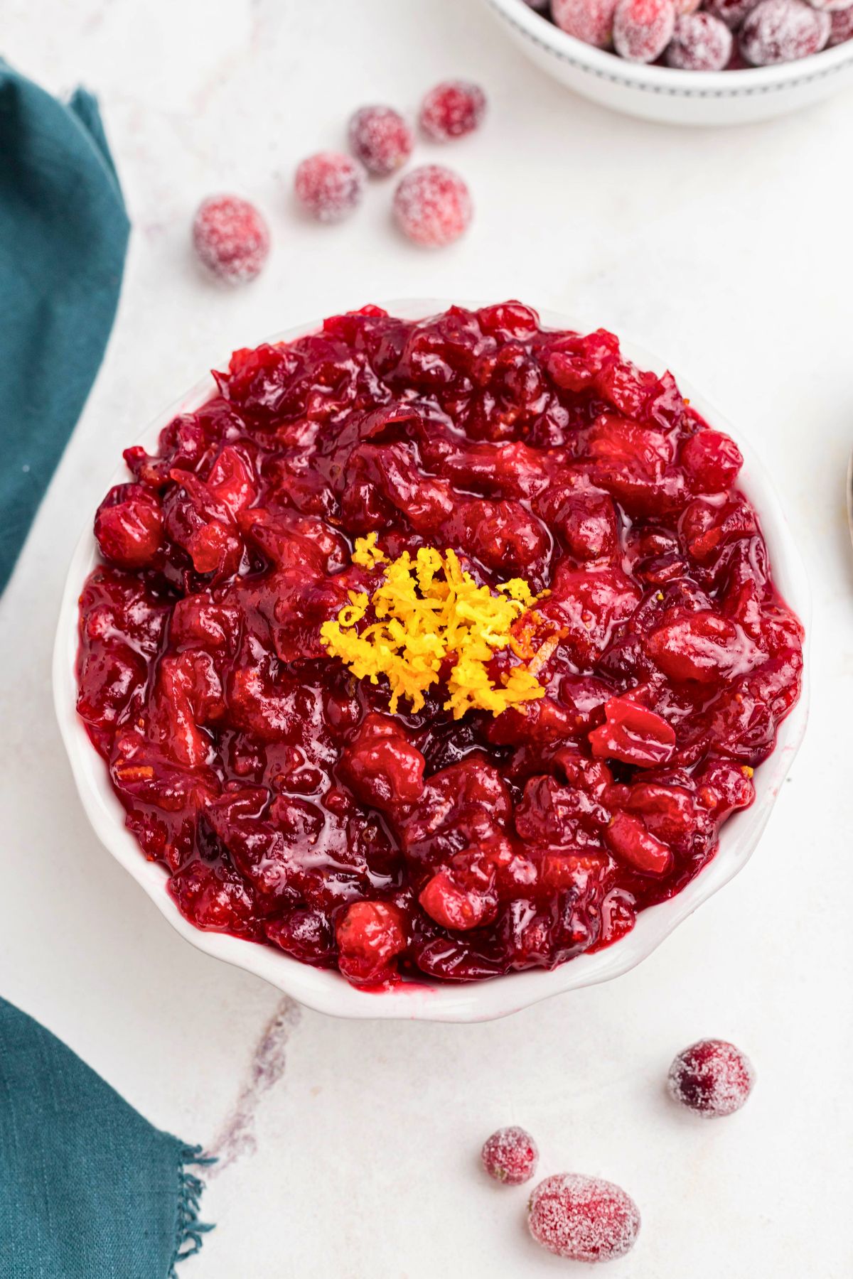 Bright red cranberry orange sauce in a white bowl with sugared cranberries on the table. 