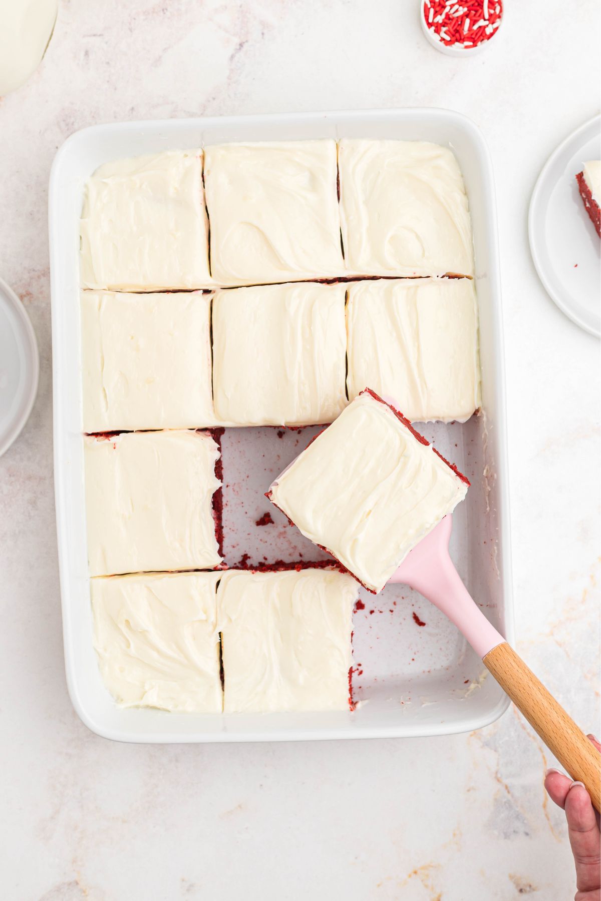 Red velvet bars in a casserole dish with cream cheese frosting on top. 