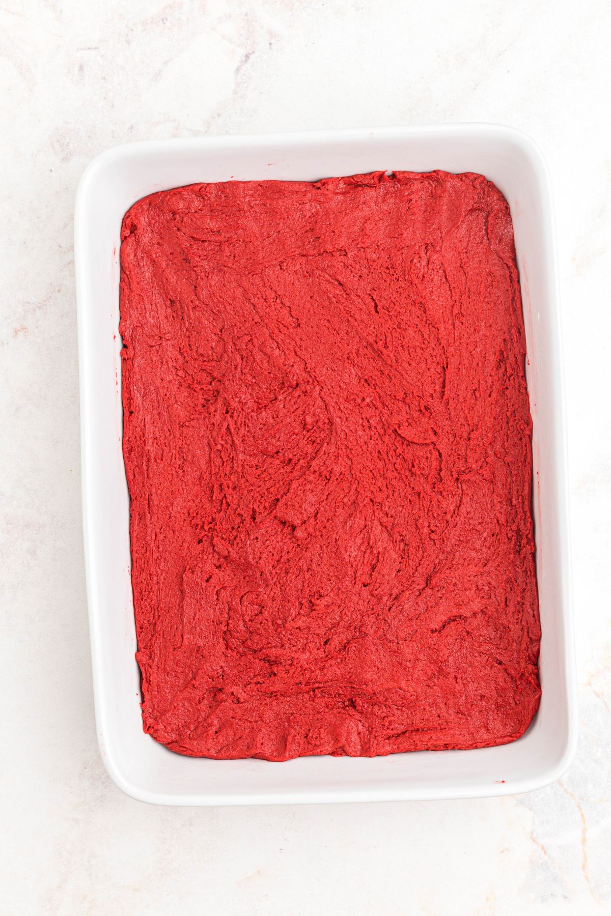 Red velvet batter in a white 9x13 pan before baking. 