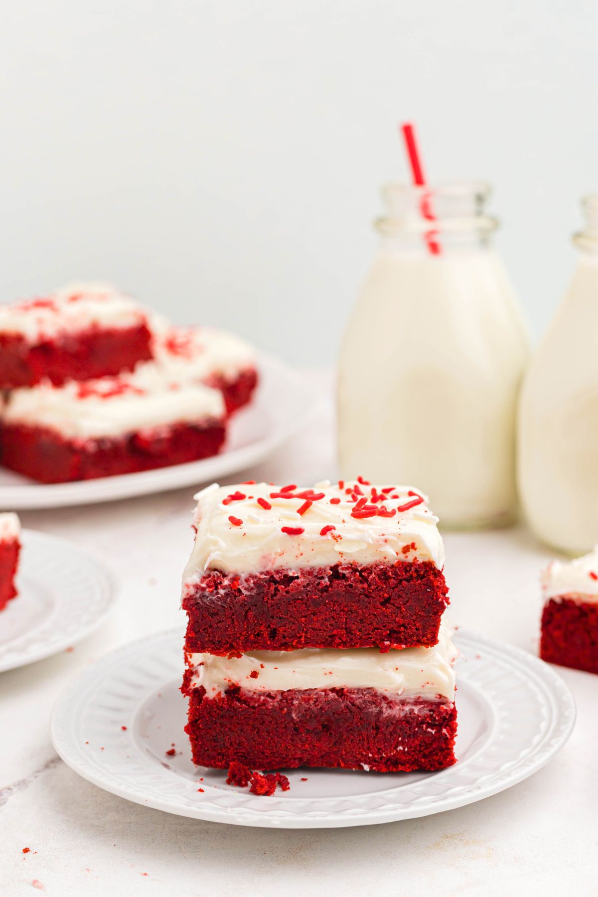 Red velvet bars frosted with cream cheese frosting, stacked on a white plate. 